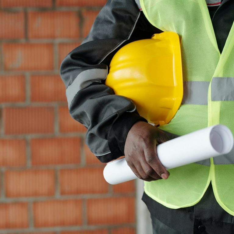 Hard Hat Photo Person wearing a yellow hard hat and reflective vest, holding construction plans.
